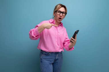 Kafkasyalı sarışın, pembe gömlek, kot pantolon ve gözlüklü, at kuyruğu saçlı güzel bir ofis çalışanı elinde akıllı bir telefon tutuyor..