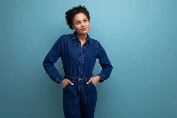 young well-groomed hispanic business woman with fluffy hair dressed in blue denim overalls isolated with copy space background.