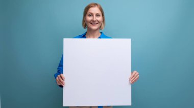 Sarışın, orta yaşlı kadın elinde not panosuyla mavi arkaplan kopyalama alanı oluşturmuş..