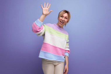 neşeli, sevimli sarışın kadın avucunu gösteriyor ve mor arka planda gülümsüyor..