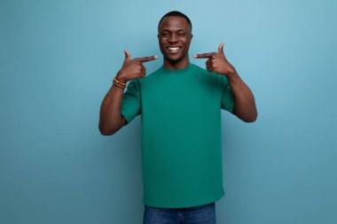 Pozitif, zeki, tişörtlü Amerikalı adam mavi arka plandaki geniş gülümsemesini fotokopi çekerek gösteriyor..