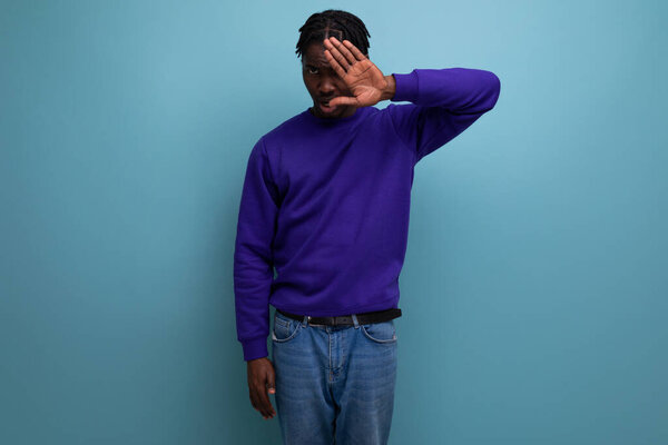 Portrait of an emotional dark-skinned african young guy in a blue sweatshirt and jeans in the studio.