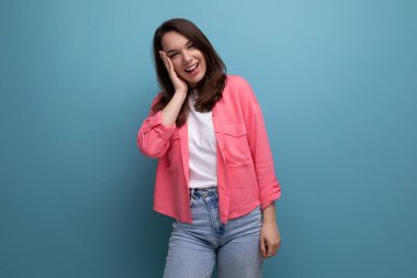 Pembe gömlekli ve kot pantolonlu genç bir kadın. Stüdyoda gülümsüyor..