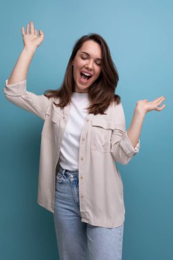 Neşeli, pozitif esmer, 30 yaşında, gömlek ve kot pantolon giymiş bir kadın gülüyor ve surat yapıyor..