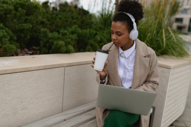 Öğrenim molasında Afrikalı genç bir kız öğrenci kulaklıkla müzik dinliyor ve kahve içiyor..