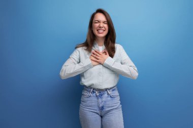 25 yaşında, kahverengi saçlı, çizgili bluz giymiş bir kadın ellerini kalbine yakın tutuyor..