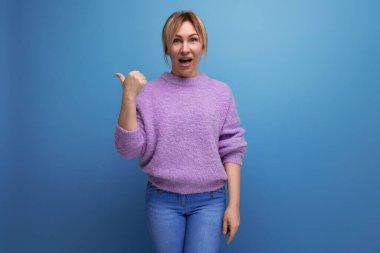 Şaşırdım. Mor kazaklı hoş sarışın kadın elini mavi arka planda fotokopi alanı olan bir yere gösteriyor..