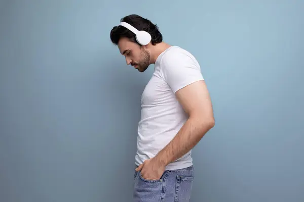 cute brutal brunette guy in a white T-shirt with headphones is dancing.