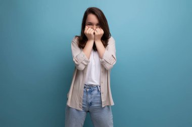 Şaşırmış 30 'lu yaşlarda, koyu renk saçlı, mavi arka planda kot pantolonlu bir kadın..