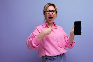 Pembe bluz ve kot pantolondan oluşan şık görünümlü at kuyruklu beyaz kadın modeli akıllı telefondan promosyon teklifini gösteriyor..