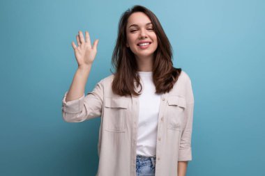 Gülümseyen 25 yaşında bir kadın. Mavi arka planda zarif bir görünüm takınıyor..