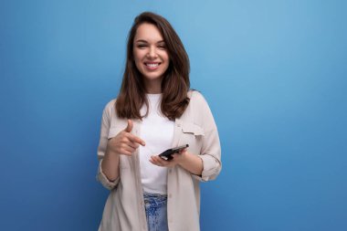 Gayri resmi giyinmiş, mavi arka planda telefonu olan hoş, koyu renk saçlı bir bayan..