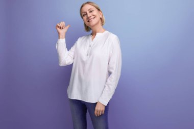 Beyaz bluzlu şık, orta yaşlı bir kadın stüdyo arka planında bir şeyler gösteriyor..