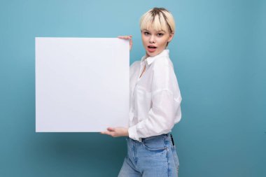 Kısa saçlı, beyaz gömlekli ve kot pantolonlu, beyaz bir pano taşıyan, beyaz saçlı, genç, pozitif beyaz bir kadın bilgi yerleştirme şablonu taşıyor. iş kavramı.