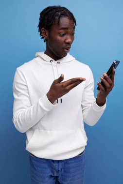 Beyaz tişörtlü Afrikalı genç adam akıllı telefondan anlıyor..