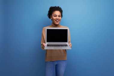 Afro kıvırcık saçlı, genç ve güzel İspanyol bir bayan. Günlük kıyafetleriyle dizüstü bilgisayarı tutuyor. Arka planda fotokopi alanı var..