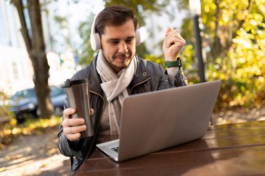 Avrupalı erkek serbest yazar, kafe terasında otururken dizüstü bilgisayardan video yayınını izliyor.