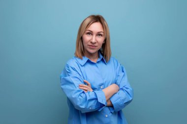 ciddi bir Avrupalı sarışın kadın ellerini önlerinde katladı mavi bir arka planda kopyalanmış boşlukta.