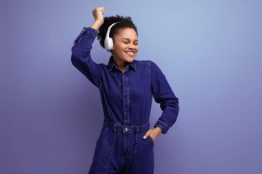 Mavi kot elbise giymiş, kablosuz kulaklıkla müzik dinleyen tüylü, neşeli İspanyol bir iş kadını..