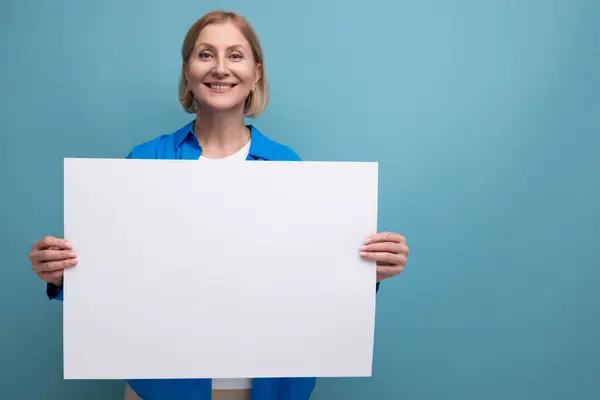 Blonde Middle Aged Woman Holding Paper Banner Mockup Blue Background Stock Photo