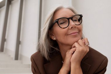 60 yaşında, bakımlı, ince saçlı, beyaz saçlı, şık giyinmiş bir iş kadını işten geçerken özgürlüğün tadını çıkarıyor..
