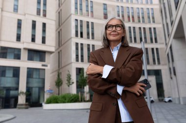 Şık takım elbiseli, beyaz saçlı, çekici, olgun bir kadın şehirde dolaşıyor..