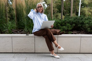 Açık tişörtlü, beyaz saçlı, narin bir girişimci kadın molada dinleniyor..