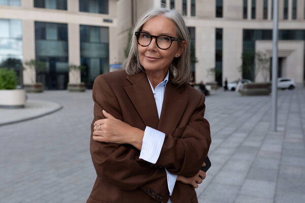 портрет ухоженной очаровательной предпринимательницы зрелых лет в коричневом костюме.