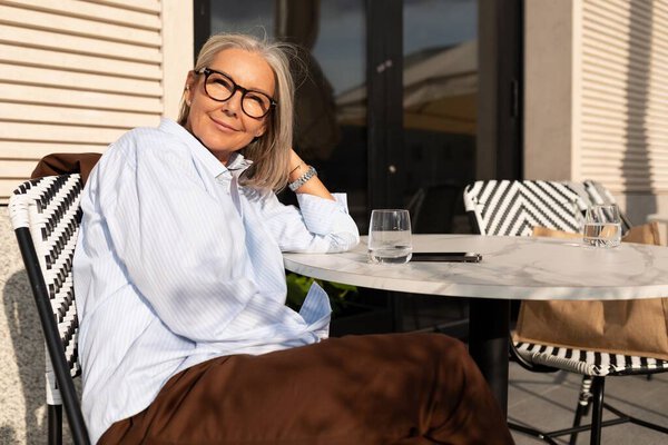 крупным планом портрет очаровательной стройной зрелой женщины с седыми волосами в стильной синей рубашке на городской улице.