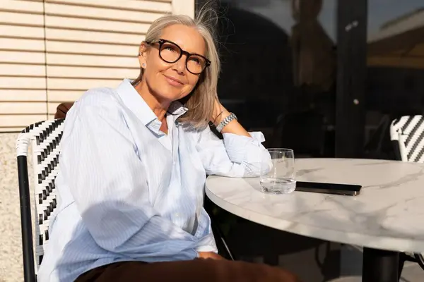 stock image business portrait of a confident successful 60 year old gray-haired woman in glasses sitting during a business lunch on the terrace.