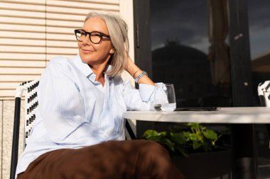 Kahve molası sırasında kafede oturan ince gri saçlı orta yaşlı iş kadınının portresi..