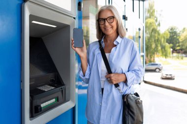 Yetişkin bir kadın, şehir caddesinde ATM 'nin yanında duruyor..