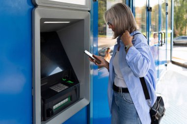 Yetişkin bir kadın, şehir caddesinde ATM 'nin yanında duruyor..