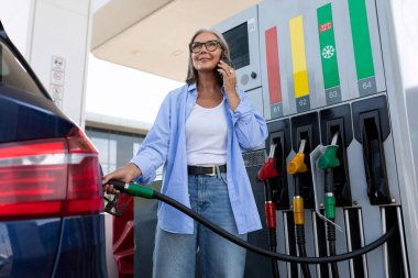 Olgun yaşlı bir kadın arabaya benzin dolduruyor..