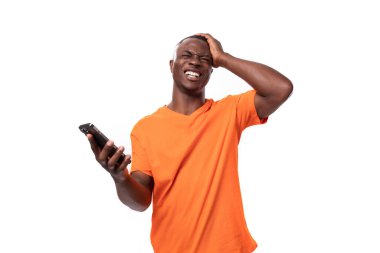 Turuncu pamuk tişört giymiş, elinde akıllı telefon tutan genç, narin bir Amerikalı..