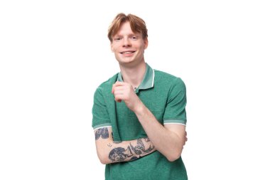Kolunda dövmesi olan, yeşil tişörtlü, kendine güvenen kızıl saçlı bir adamın portresi..