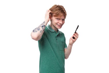 Yeşil tişört giymiş genç kızıl saçlı adam arka planda fotokopi alanı olan bir akıllı telefon kullanıyor..