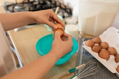 Bir kadın mutfakta dururken kasede tavuk yumurtası kırar..