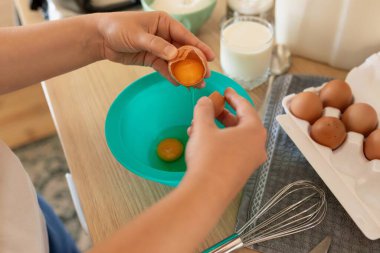 Bir kadın mutfakta dururken kasede tavuk yumurtası kırar..