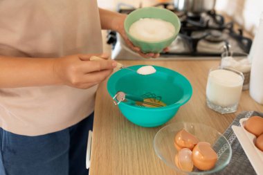 Bir kadın mutfakta krep pişirmek için hamur malzemesi ekliyor..