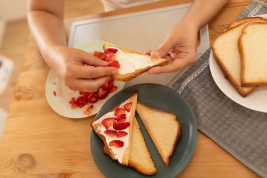 Üst manzara, bir kadın tostun üzerine ekşi krema sürüyor ve üzerine çilek koyuyor..