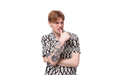 Kırmızı saçlı, kısa kollu gömlekli, beyaz arka planda poz veren genç ve zeki bir adam..