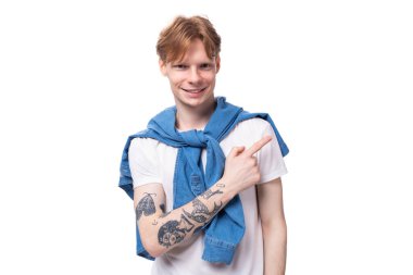 Genç, kısa saçlı, sarı kızıl saçlı, kollarında dövmesi olan beyaz bir erkek öğrenci elini yana doğru gösteriyor. reklam kavramı.