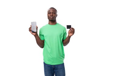 Genç Amerikalı adam yeşil tişört giyip akıllı telefon ekranı ve kredi kartı gösteriyor..