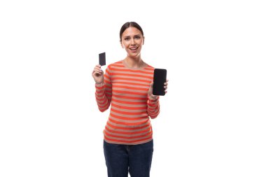 Turuncu kazak giymiş genç ve güzel bir kadın elinde plastik bir kart ve reklam amaçlı akıllı bir telefon tutuyor..