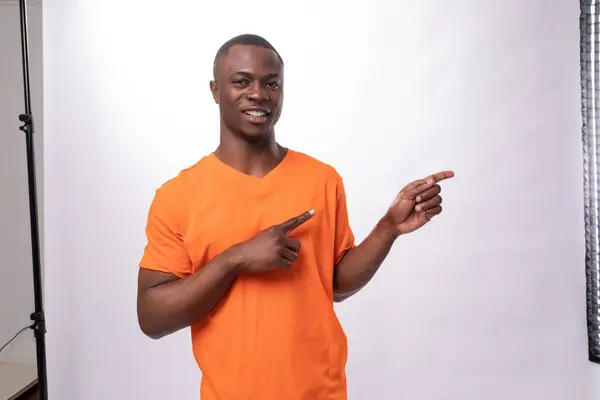 young american man dressed in orange t-shirt with print mockup pointing with finger at news.