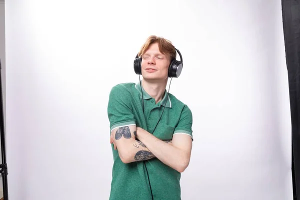 穿着绿色T恤的年轻英俊红头发男人喜欢听耳机里的音乐 而且听起来很兴奋 — 图库照片