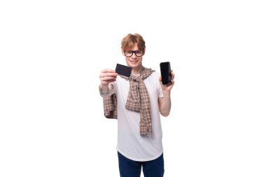 Kafkasyalı, kırmızı saçlı, elinde kredi kartı modeli ve akıllı telefon tutan genç bir adam..