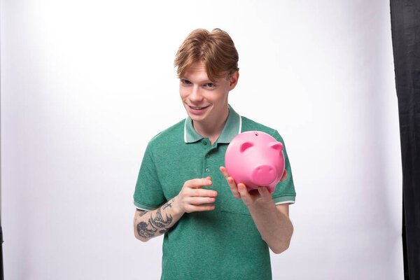 a young red-haired caucasian guy in a green t-shirt is about to empty his piggy bank.
