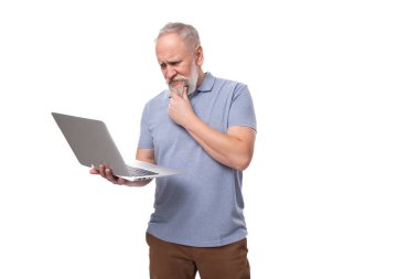 Gri saçlı, sakallı, bıyıklı, tişörtlü ve pantolonlu olgun bir adamın elinde dizüstü bilgisayar var..